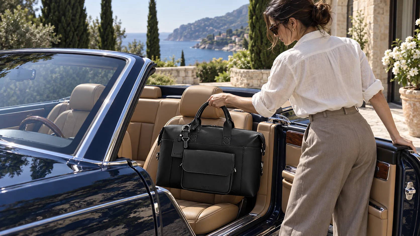 A woman placing the black SVOLTA travel bag on the passenger seat of an open-top blue convertible beside a Mediterranean villa